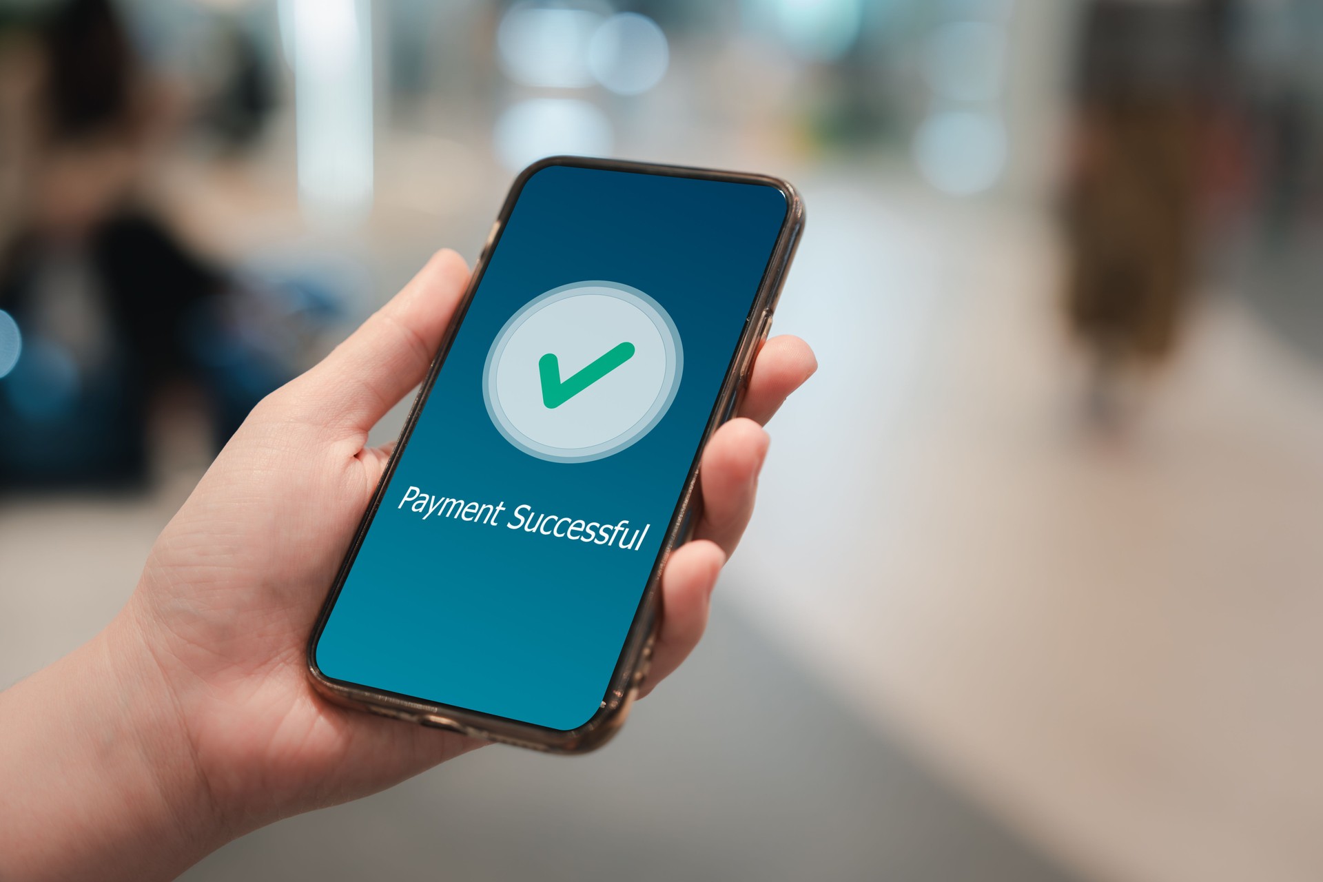 Teléfono móvil de mano y aplicación que muestra el mensaje de pago exitoso con marca de verificación verde.